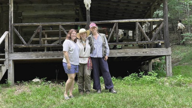 Chelsea, Phyllis, and Lisa stand in front of an old structure in the forest
