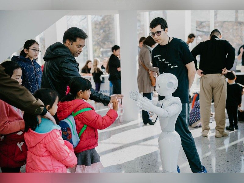 Caption: Adult man and young girl holding up hands to greet robot with arms outstretched at the 2019 Virginia Tech Science Festival.  