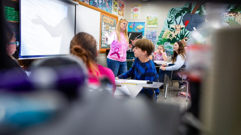 Elementary students in a classroom listening to their teacher.